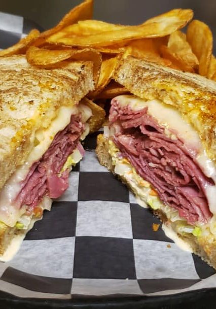 A reuben sandwich with fries on a checkered plate.
